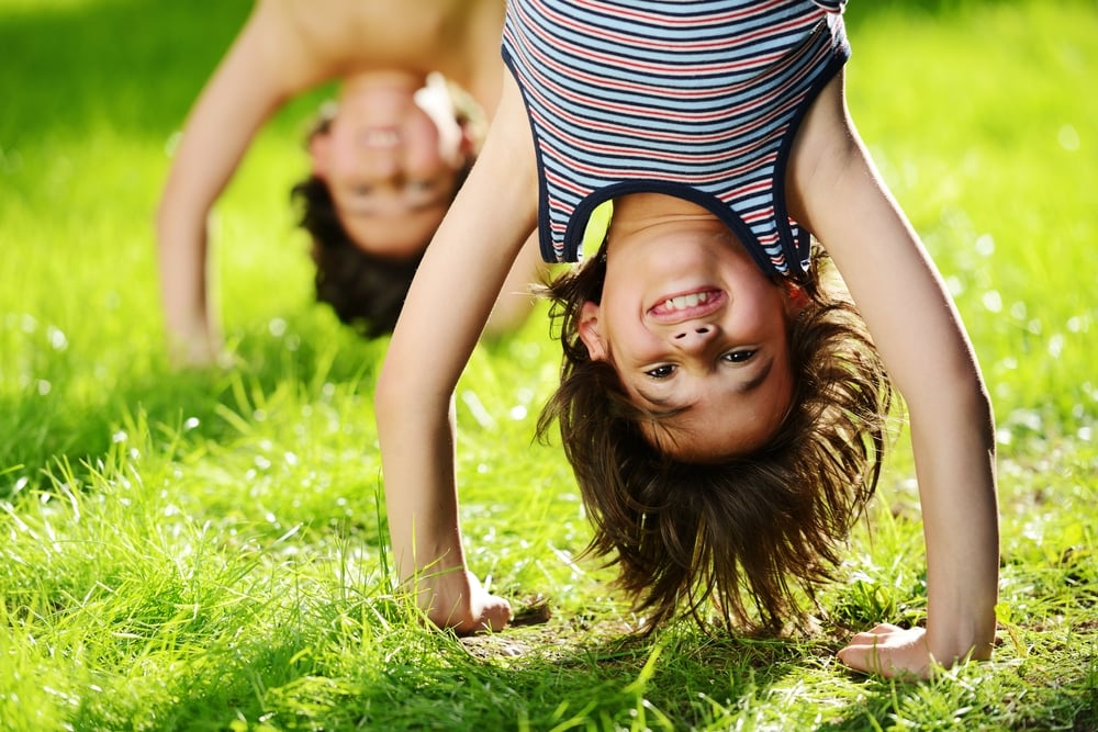 Portraits of happy kids playing upside down outdoors in summer park